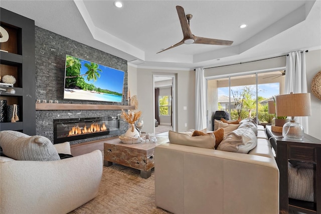 living room with ceiling fan, built in features, a fireplace, and a tray ceiling