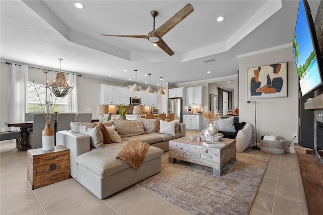 tiled living room featuring a tray ceiling, a high end fireplace, ceiling fan with notable chandelier, and ornamental molding