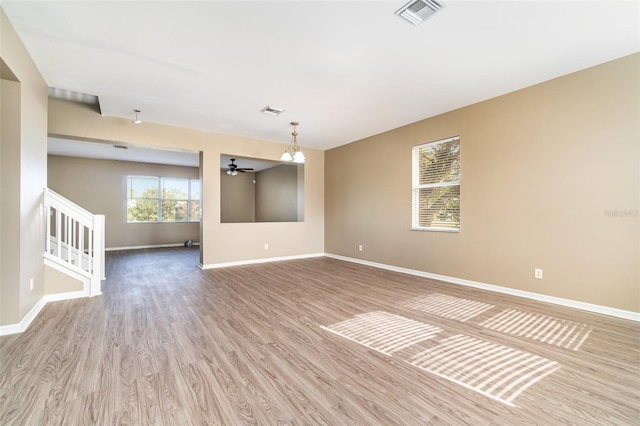 spare room with ceiling fan with notable chandelier and light hardwood / wood-style flooring