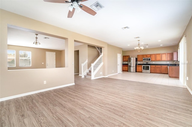 unfurnished living room with sink, ceiling fan with notable chandelier, and light wood-type flooring