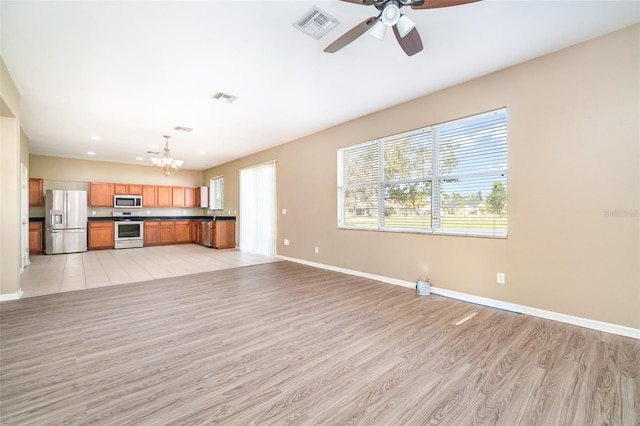 unfurnished living room featuring ceiling fan with notable chandelier, a wealth of natural light, and light hardwood / wood-style flooring