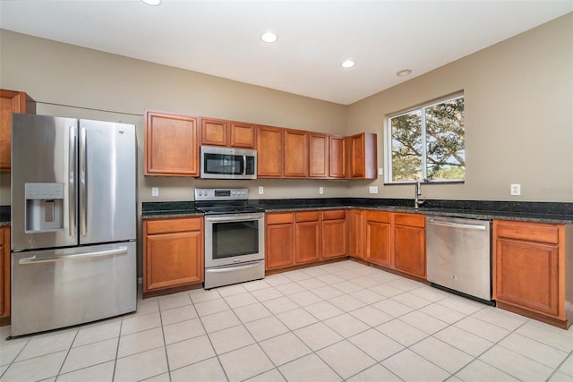 kitchen with light tile patterned flooring, sink, appliances with stainless steel finishes, and dark stone counters