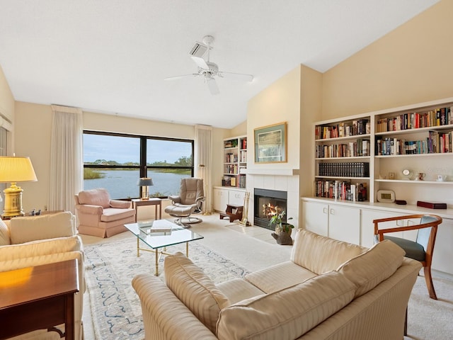 carpeted living room with a water view, a tiled fireplace, ceiling fan, and lofted ceiling