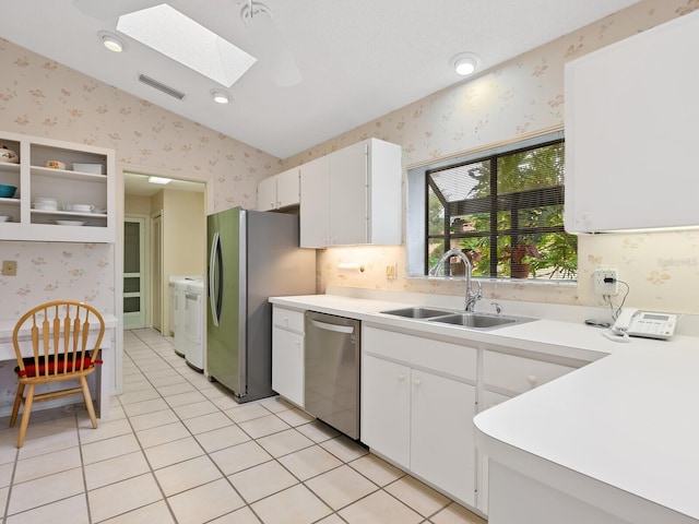 kitchen featuring light tile patterned floors, white cabinetry, appliances with stainless steel finishes, vaulted ceiling with skylight, and sink