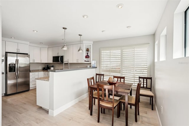 kitchen with kitchen peninsula, appliances with stainless steel finishes, light hardwood / wood-style flooring, white cabinets, and hanging light fixtures