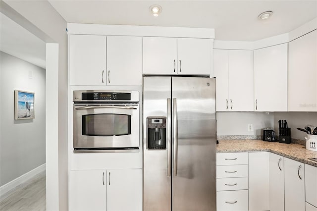 kitchen with light stone countertops, stainless steel appliances, white cabinetry, and light hardwood / wood-style flooring