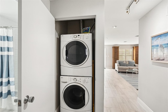 laundry room featuring stacked washer / dryer and track lighting