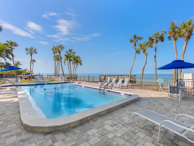 community pool featuring a patio area, a water view, and fence