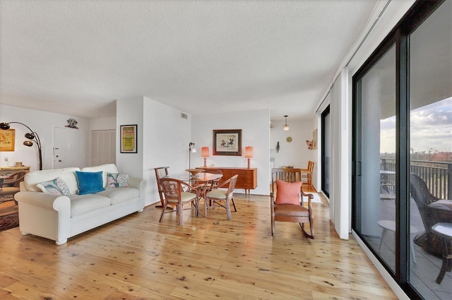 living area featuring light wood-type flooring, visible vents, and a textured ceiling