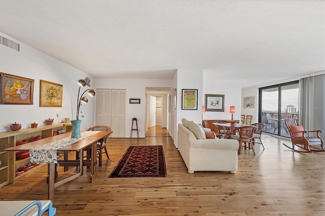 living area with a wall of windows, visible vents, a textured ceiling, and wood finished floors