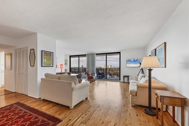 living room featuring a textured ceiling, a wall of windows, and light wood-type flooring