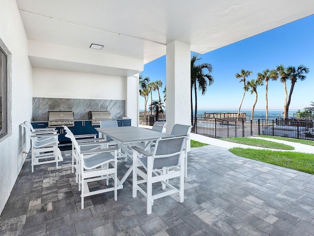 view of patio / terrace with outdoor dining area, an outdoor kitchen, a water view, fence, and grilling area