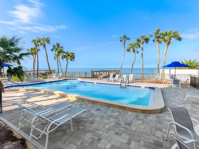 community pool with a water view, a patio area, and fence