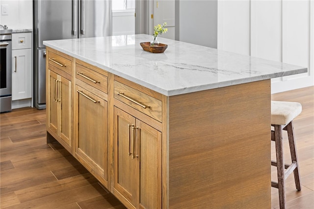 kitchen featuring light stone countertops, hardwood / wood-style flooring, a center island, a breakfast bar, and high quality fridge