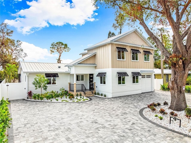 view of front of property with decorative driveway, board and batten siding, a gate, fence, and metal roof