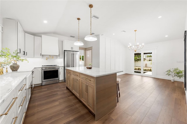 kitchen with stainless steel appliances, white cabinets, vaulted ceiling, light stone countertops, and a kitchen island