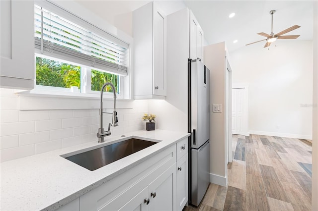 kitchen with sink, white cabinets, light stone counters, and stainless steel fridge