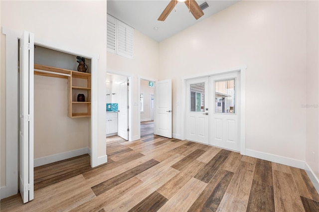 unfurnished bedroom with ceiling fan, light wood-type flooring, a closet, and a high ceiling