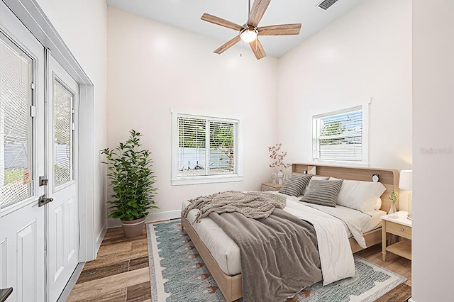 bedroom with baseboards, visible vents, light wood-style flooring, ceiling fan, and a high ceiling