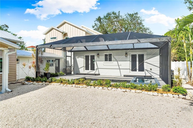 rear view of house featuring a patio, glass enclosure, fence, french doors, and board and batten siding