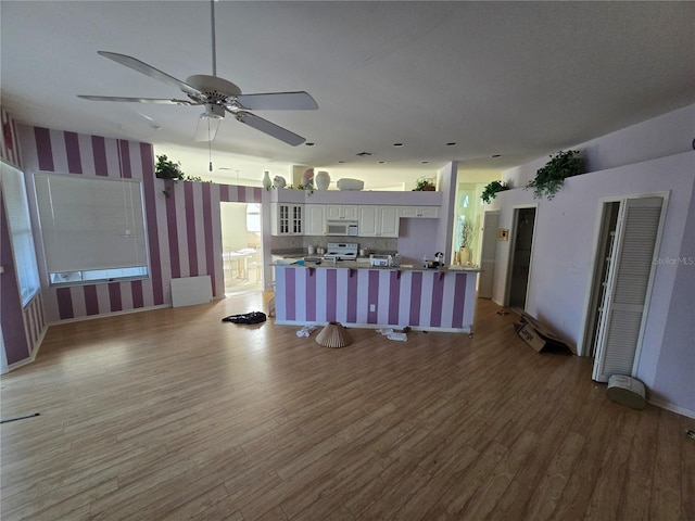 kitchen featuring kitchen peninsula, light wood-type flooring, a breakfast bar, electric stove, and white cabinetry