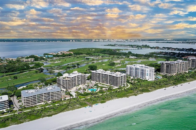 aerial view at dusk featuring a water view and a beach view