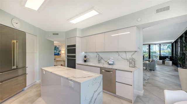 kitchen featuring backsplash, stainless steel appliances, sink, a center island, and white cabinetry