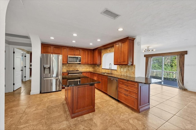 kitchen with sink, tasteful backsplash, dark stone countertops, appliances with stainless steel finishes, and a kitchen island