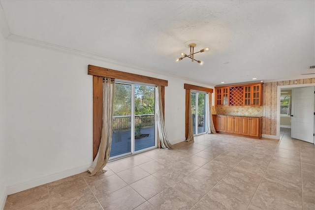 unfurnished living room with crown molding, bar, a textured ceiling, and a notable chandelier