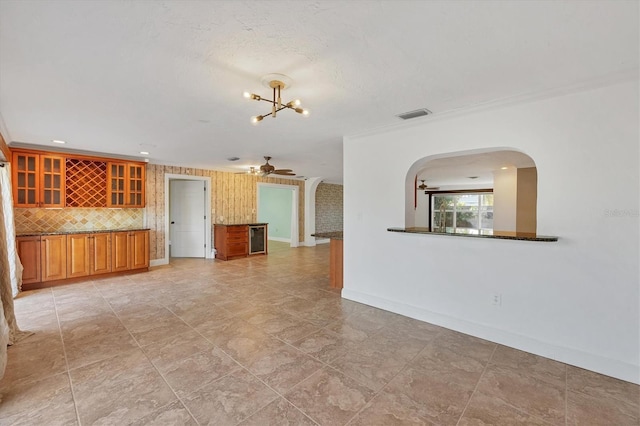 unfurnished living room with crown molding, ceiling fan with notable chandelier, and a textured ceiling