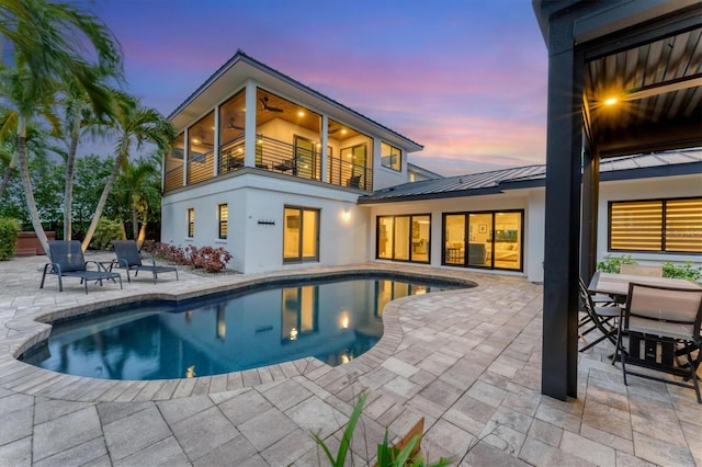 pool at dusk featuring ceiling fan and a patio