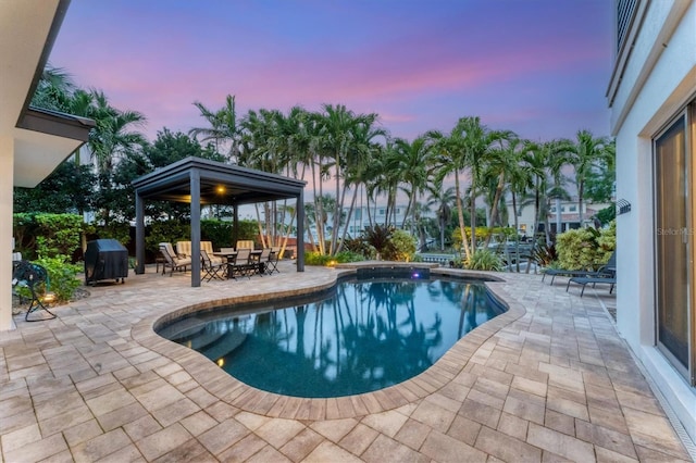 pool at dusk featuring area for grilling and a patio