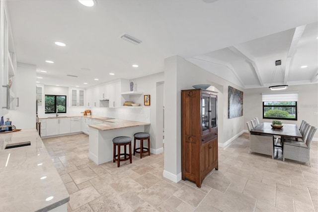 kitchen featuring kitchen peninsula, white cabinets, vaulted ceiling, and light stone countertops