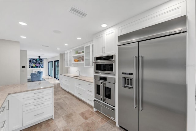 kitchen with white cabinets, appliances with stainless steel finishes, light stone countertops, and sink