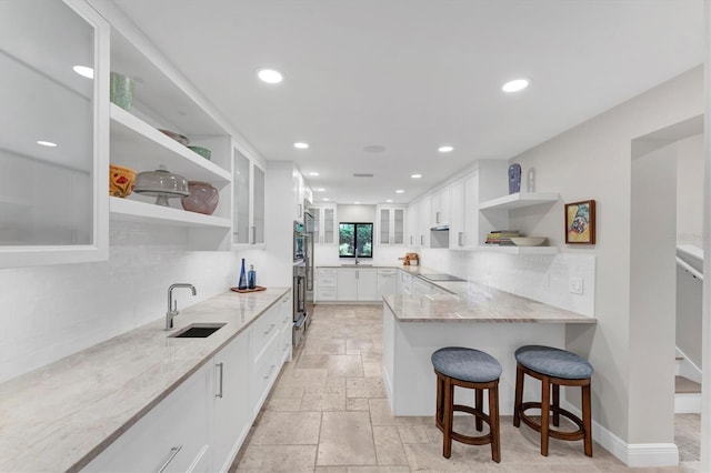 kitchen with black electric stovetop, light stone countertops, white cabinetry, and sink