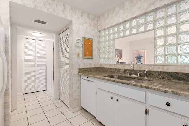 kitchen with light tile patterned flooring, sink, white cabinetry, stone countertops, and white dishwasher