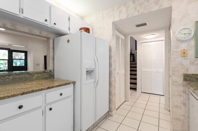 kitchen featuring dark stone countertops, light tile patterned floors, white fridge with ice dispenser, and white cabinets