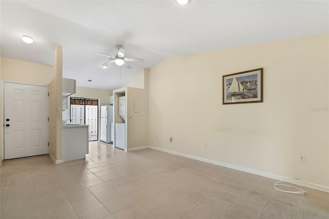 tiled spare room featuring ceiling fan, stacked washer and dryer, and vaulted ceiling