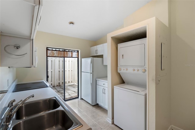 kitchen featuring stove, sink, white refrigerator, stacked washer and dryer, and white cabinetry