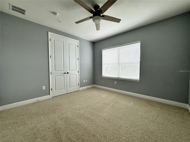 unfurnished bedroom featuring ceiling fan, a closet, light carpet, and a textured ceiling