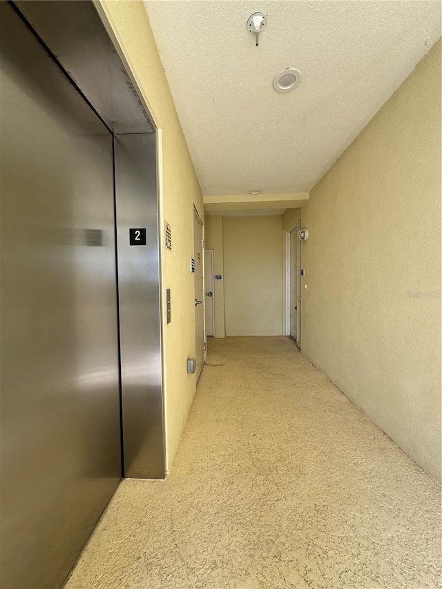 hall with elevator and a textured ceiling