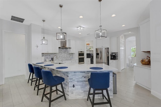 kitchen with decorative light fixtures, white cabinetry, stainless steel appliances, and wall chimney range hood