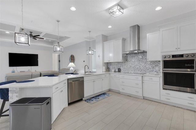 kitchen featuring wall chimney range hood, sink, ceiling fan, appliances with stainless steel finishes, and white cabinetry