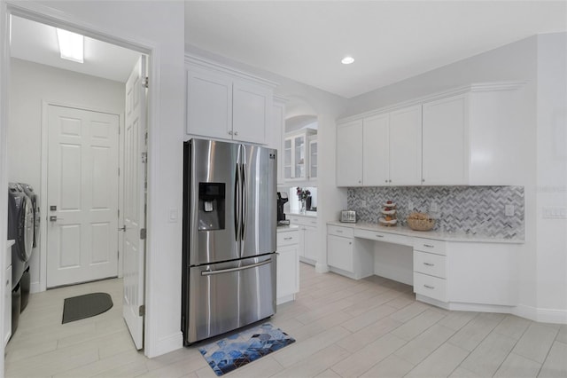 kitchen with backsplash, white cabinetry, washer and dryer, and stainless steel refrigerator with ice dispenser