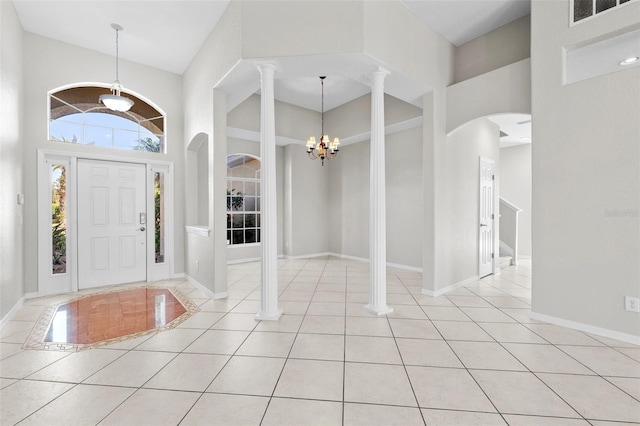 entrance foyer featuring ornate columns, a towering ceiling, light tile patterned floors, and a notable chandelier