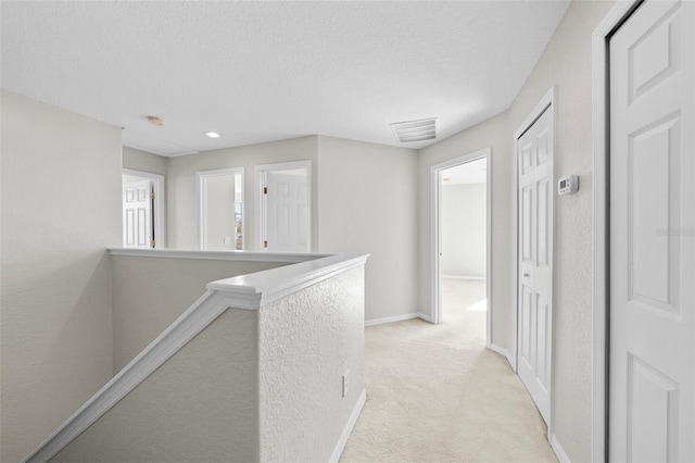 hall with light colored carpet and a textured ceiling