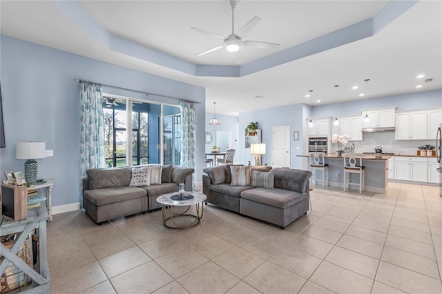 living room with a tray ceiling, ceiling fan, and light tile patterned floors