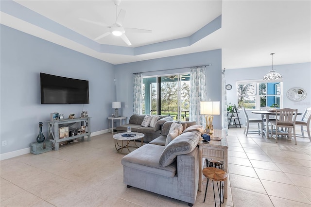 living room with ceiling fan, a raised ceiling, and light tile patterned floors