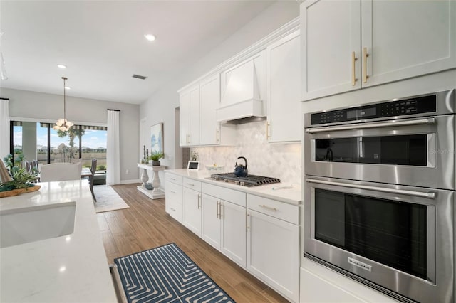 kitchen with light stone countertops, custom exhaust hood, stainless steel appliances, sink, and white cabinetry