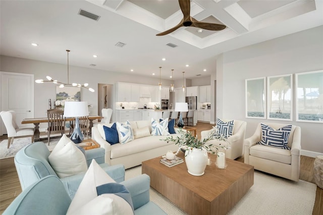 living room with beam ceiling, light hardwood / wood-style flooring, ceiling fan with notable chandelier, and coffered ceiling